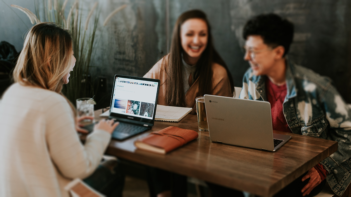 Three female students laugh while working on their laptops.