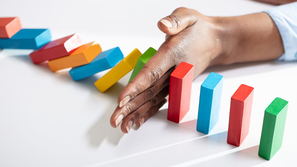 Black woman stops a series of dominoes from falling with her hand