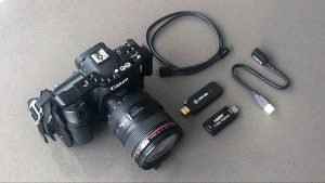 A Canon DSLR camera sits beside two capture card USB ports and a Micro-B and USB-C cord.