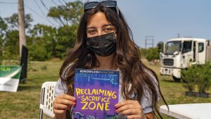 Borderless Magazine Engagement Reporter Diane Bou Khalil holds the magazine’s award-winning bilingual comic book, Reclaiming the Sacrifice Zone, while tabling at an event on Chicago’s Southeast Side in 2021. Photo: Oscar Sanchez
