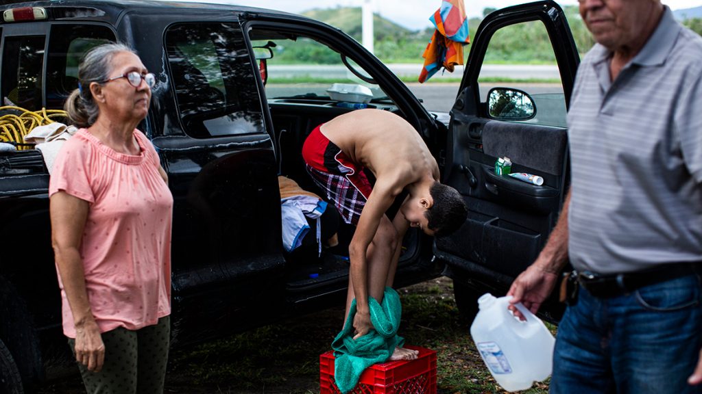 Annie Mercado, 62, and Rafael Torres, 71, help their grandson, Yonatan Elí García, 10, bathe outside an encampment next to the 166 road in Guánica, Puerto Rico on Jan. 8, 2020. They have been staying in the area since the island was hit with a 6.4 magnitude earthquake Jan. 7, the second major shake that week, leaving significant structural damage throughout the south. Photo: Erika P. Rodriguez