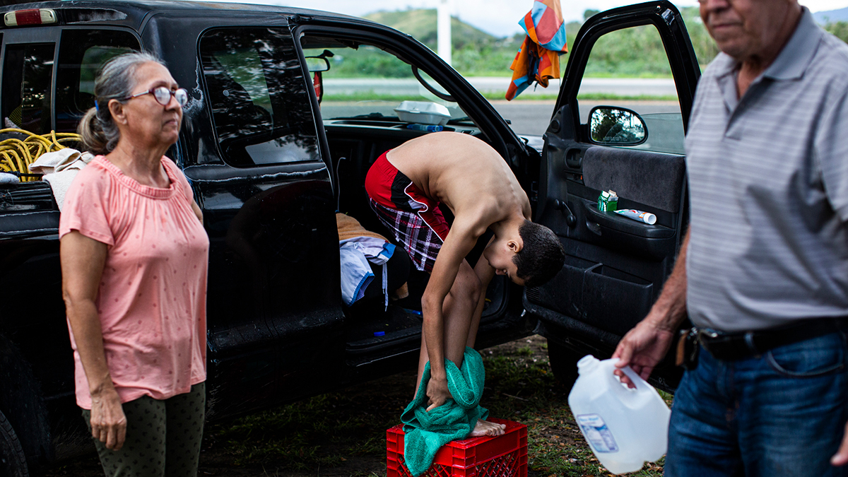 Annie Mercado, 62, and Rafael Torres, 71, help their grandson, Yonatan Elí García, 10, bathe outside an encampment next to the 166 road in Guánica, Puerto Rico on Jan. 8, 2020. They have been staying in the area since the island was hit with a 6.4 magnitude earthquake Jan. 7, the second major shake that week, leaving significant structural damage throughout the south. Photo: Erika P. Rodriguez