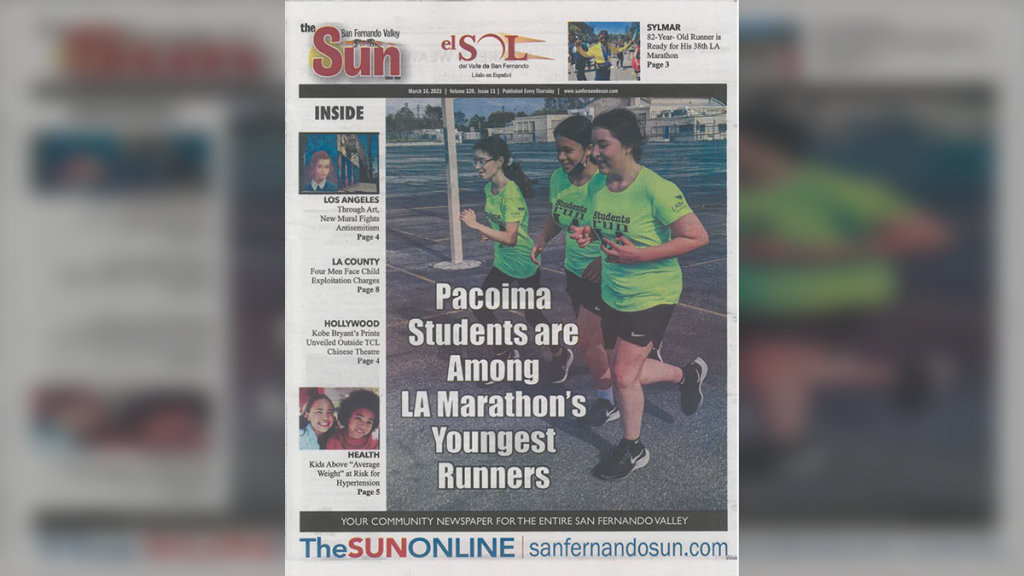 A photo of the front page of the San Fernando Valley Sun. The front page has a large photo of people running on the right center, with white box letter text reading "Pacoima Students are Among LA Marathon's Youngest Runners." Above the photo is a black box with the date, issue number and website. At the top are the Sun's two logos: one in English and one in Spanish. There is also a teaser in the right upper corner and down the left side of the page. The bottom of the page contains a link to the Sun's website in blue.