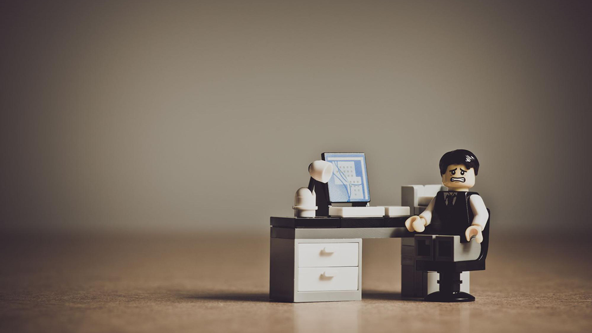 A Lego toy desk with a distressed Lego business man sitting in a chair