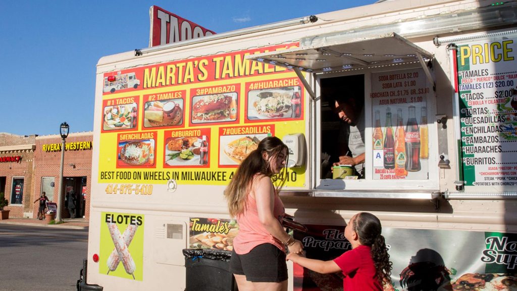 Woman with a young girl outside a Marta's Tamales food van with a menu on the side.