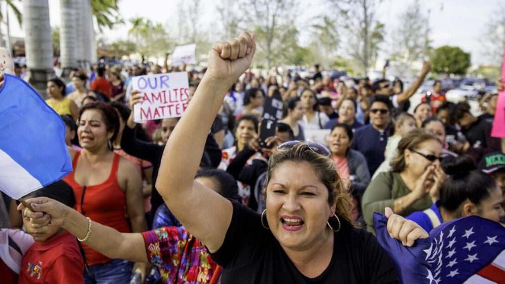 Photo of a gathering in a Latino community featuring a woman raising her fist in the air and a person holding a sign saying, "Our families matter."