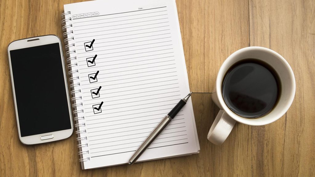 A phone, a notepad and a cup of coffee on a table top