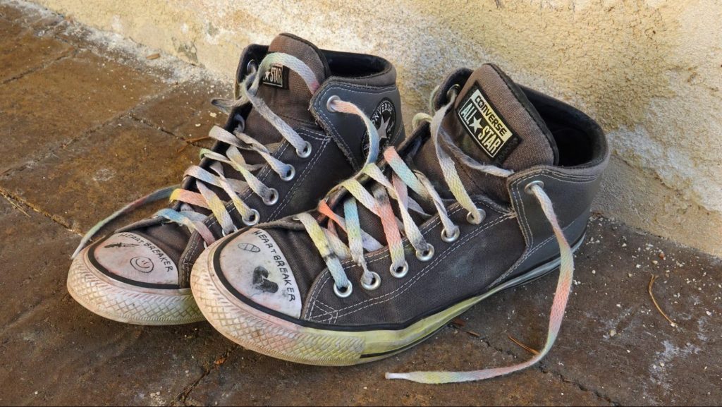 A teen's well-worn, drawn on Converse All-Star sneakers, with the laces painted in rainbow colors for gay pride.