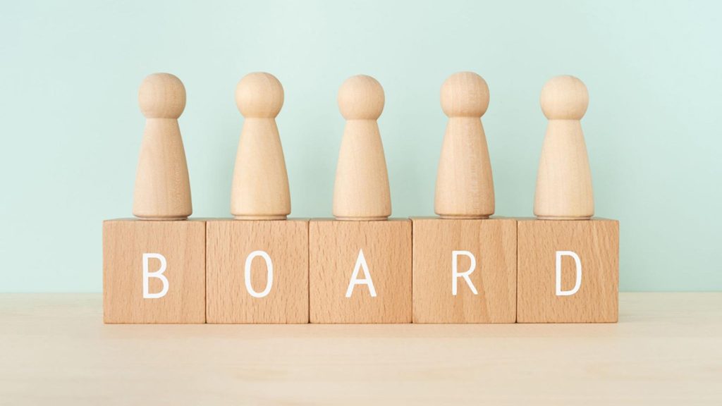 Wooden blocks spell out BOARD with wooden game pieces on top of each.