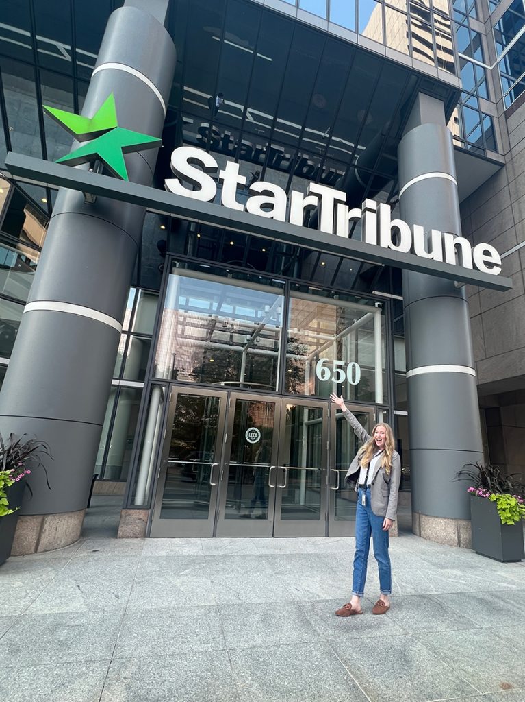 Emily Hood standing in front of the Star Tribune sign in downtown Minneapolis