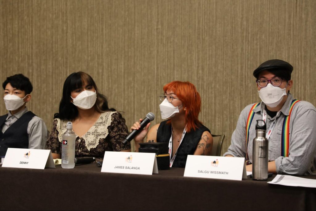 Me at an AAJA panel this year with an N95 and air purifier — mitigations that made the experience safer thanks to panelists all masking, providing extra masks, and panel moderator Salgu Wissmath including a slide emphasizing the importance of masking for community safety. Photo courtesy of Naomi Ishisaka.