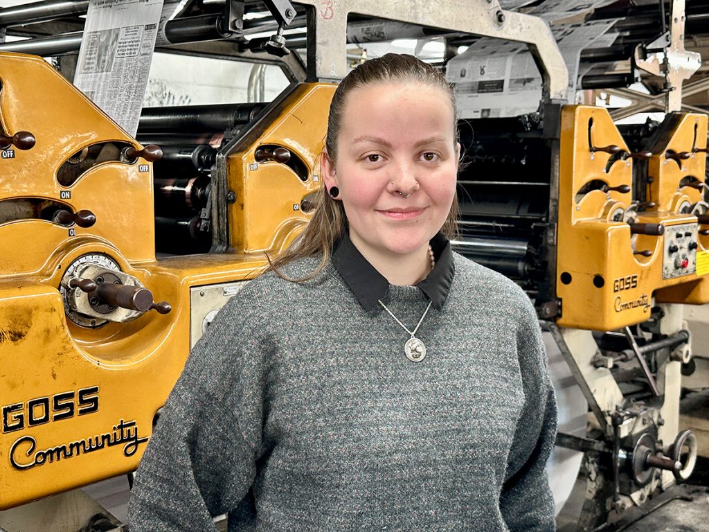 Genevieve Smith stands next to the printing presses of The Advertiser in Eldon, Missouri.