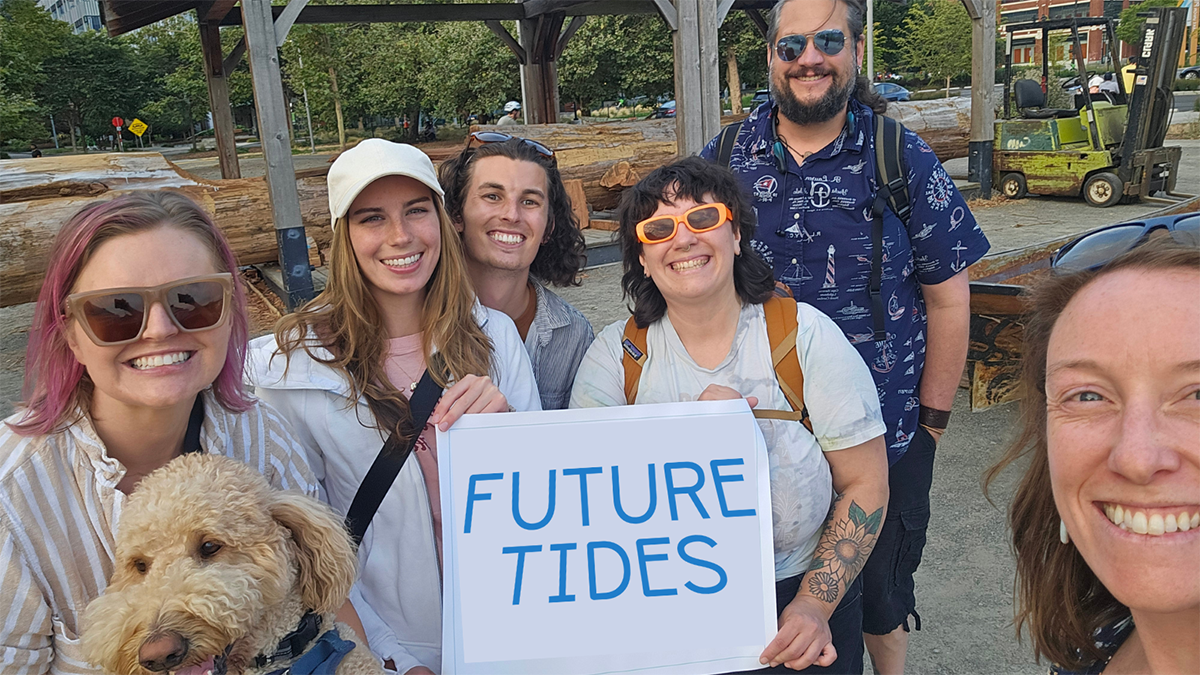 Cara Kuhlman (right) leads a walking tour for her news outlet, Future Tides. Tour participants hold a sign reading “Future Tides.”