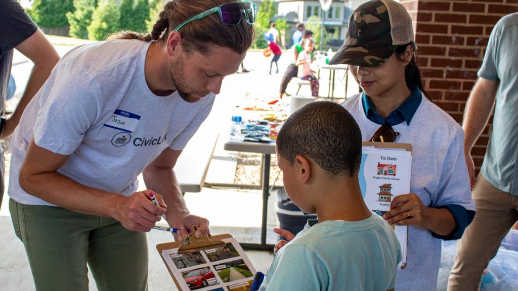 Man shows clipboard with photos to a boy while a woman holding a clipboard looks on.