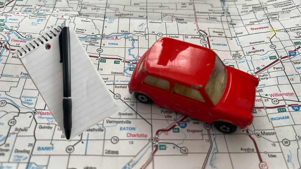 Red toy car and writer's notebook on a road map. Red toy car and writer's notebook on a road map.