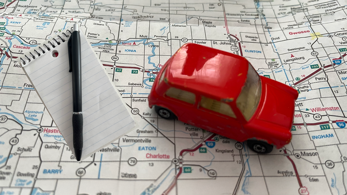 Red toy car and writer's notebook on a road map.