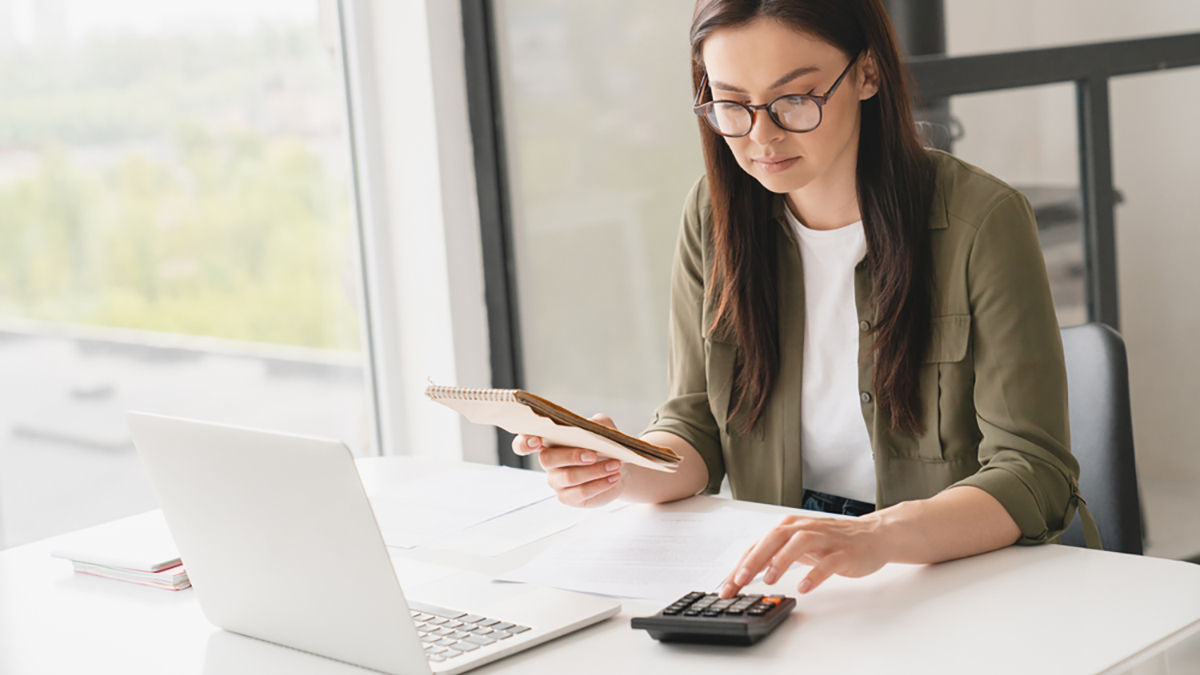 Young caucasian business woman counting funds, planning budget, paying bills online using calculator. Freelancer boss CEO doing paperwork with finances.