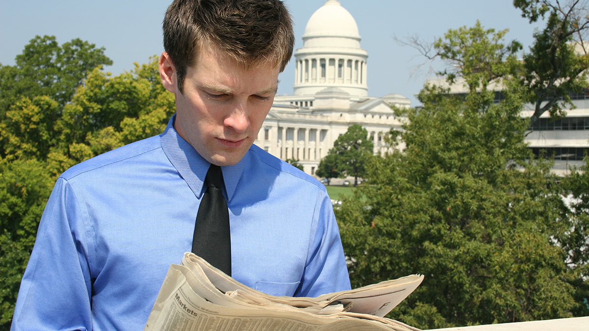 Man in front of a government building reading a newspaper.