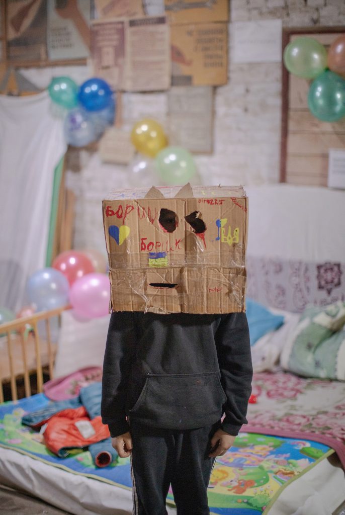 Child with a cardboard box over their head in a room decorated with balloons