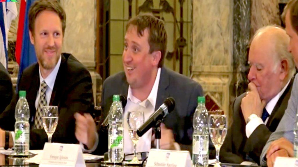 APU President Fabián Cardozo, center, explains the impact of having Enrique V. Iglesias, right, as a supporting force for the Ethical Pact initiative during the signing ceremony for the pact against misinformation at the Legislative Palace on April 26, 2019. At left, Stefan Liller, UNDP representative in Uruguay during that period. Photo from video | Courtesy: De fogón en fogón