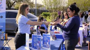 A woman hands something to another woman at a local community event.