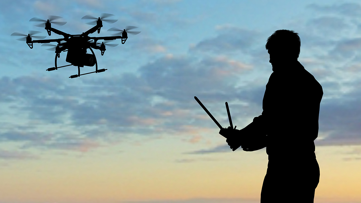 Man flying a drone with a controller at sunset
