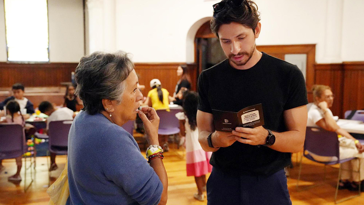 Rommel H. Ojeda, Documented’s Senior Community Correspondent, right, shares a printed guide with an attendee. Photo: April Xu