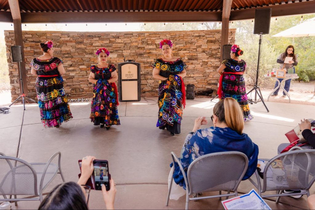 Four Hispanic women in cultural costume dancing before an audience